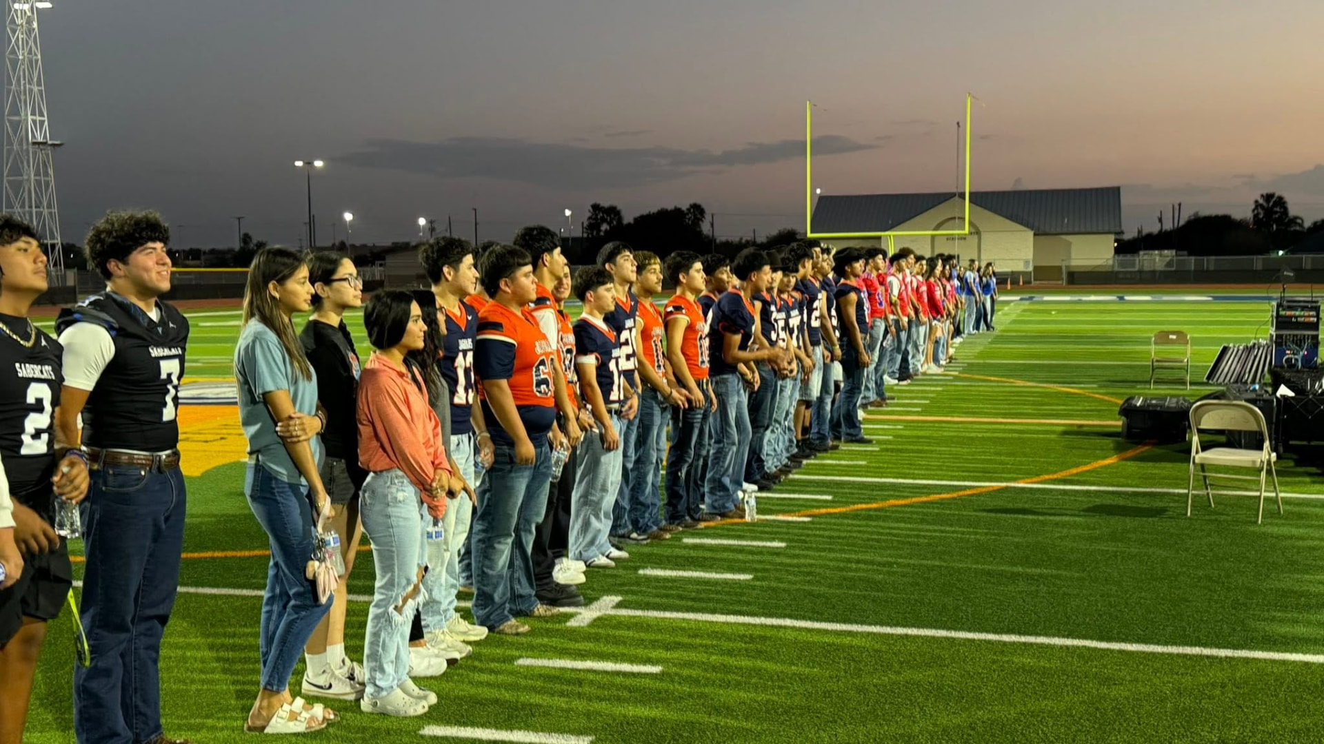 Football players from multiple Edinburg, Texas schools standing in a line on the field at sunset